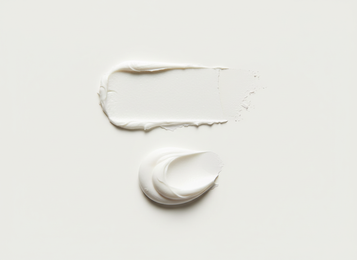 Two smears of white cream on a light gray background